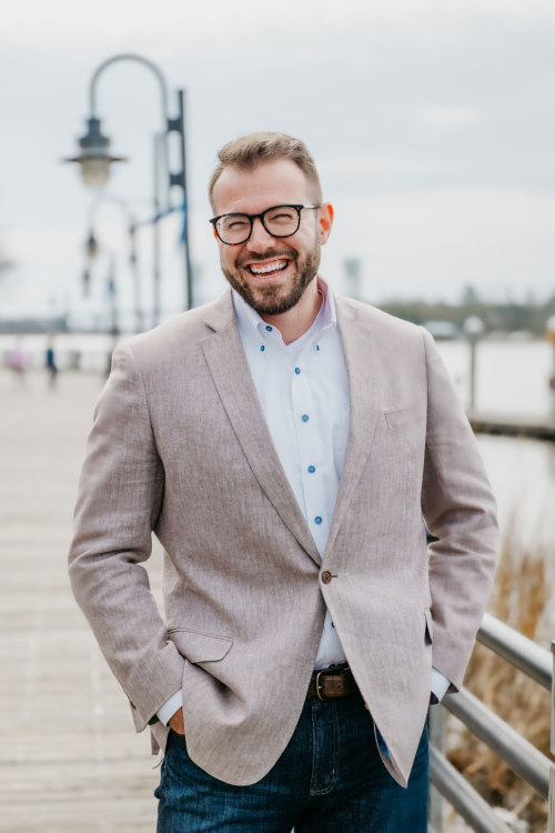 A man in glasses and a jacket standing on the pier.